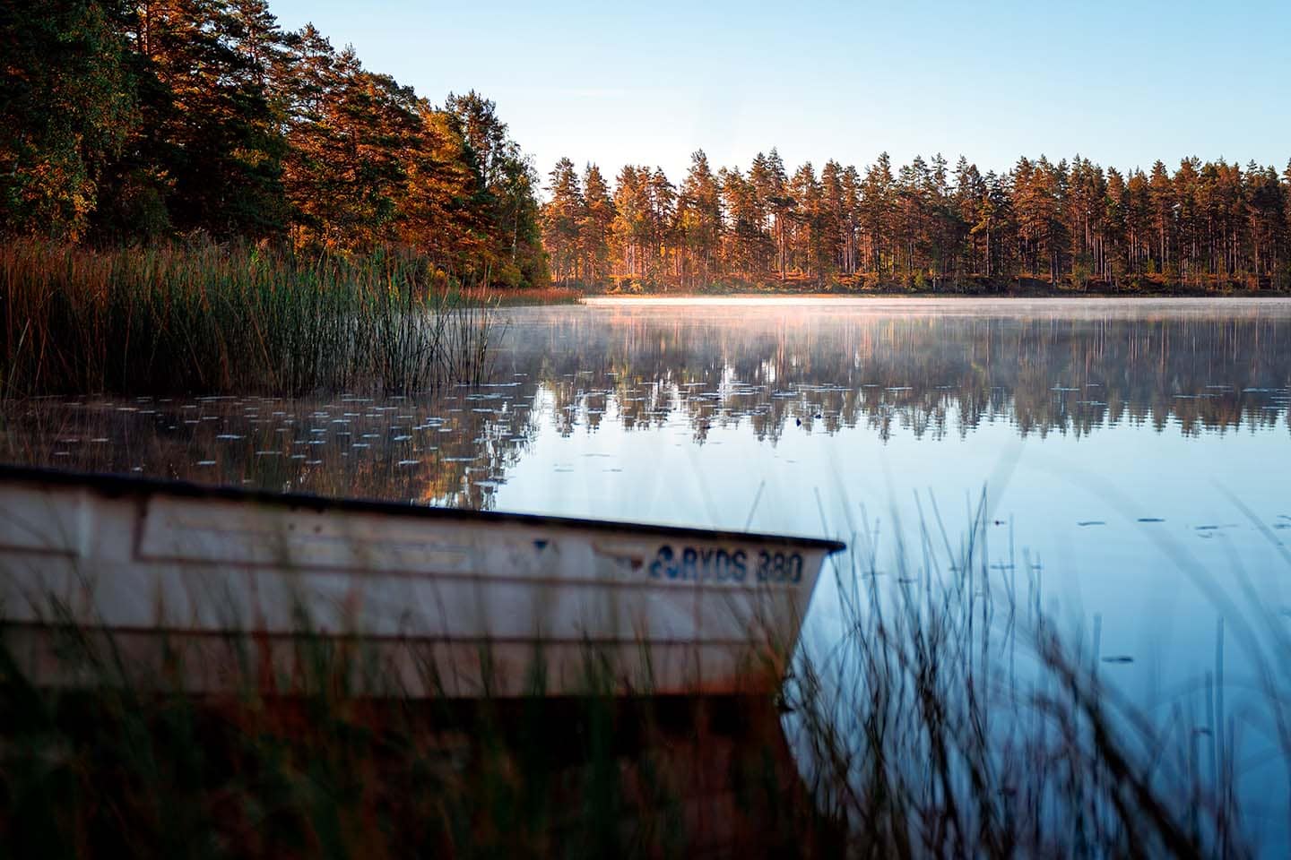 swedish lake with mist and sunset and boat in foreground