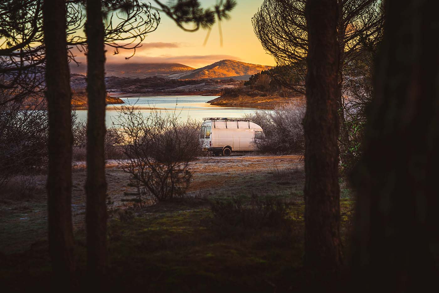 looking through trees at campervan at sunset in Spains Cantabrian Mountains. Lake and hills in the background