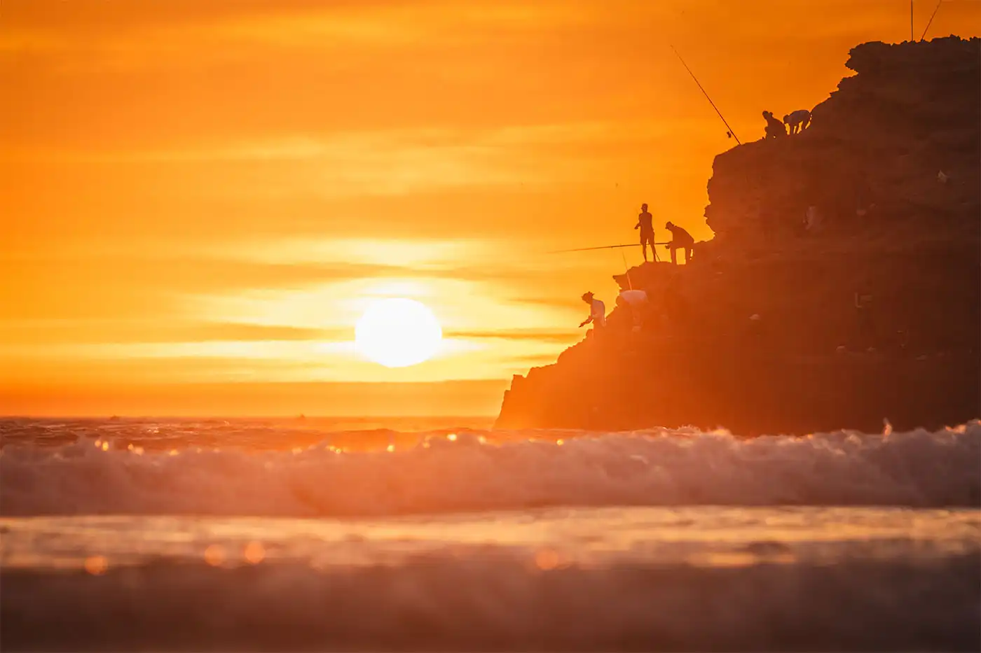 people fishing on rocky outcrop at sunset